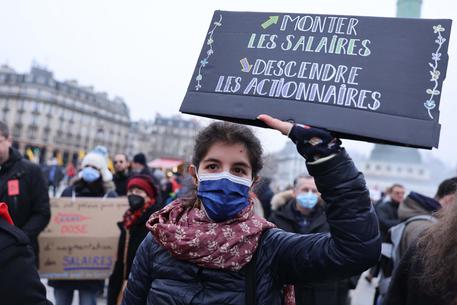 A protestor holds a sign reading "Rise the salaries and getting down the shareholders" during a demonstration to defend public services, education, wages and pension in Paris on January 27, 2022. (Photo by Thomas SAMSON / AFP)
